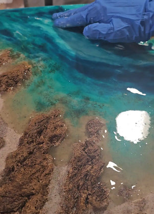 Detalle del proceso de elaboracion del cuadro de resina Playa de Barrika, manos con guantes modelando las rocas hecho a mano en Bizkaia