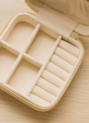 Interior del joyero de viaje Qordatta con compartimentos para joyas, porta anillos y bolsillo, forro aterciopelado crema