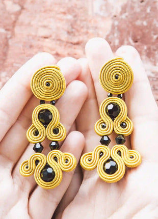 Manos sosteniendo pendientes Versalles de soutache mostaza hechos a mano en Bizkaia, regalo original para mujer unico e irrepetible