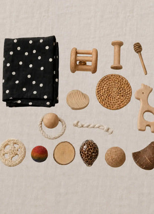 Contenido de la Cesta Tesoros Natura Montessori: sonajeros de madera, tela de lunares, objetos de distintas texturas y materiales naturales para la estimulación sensorial del bebé